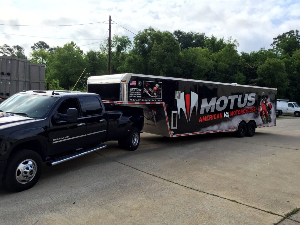 Black pickup towing the wrapped Motus Motorcycles gooseneck trailer