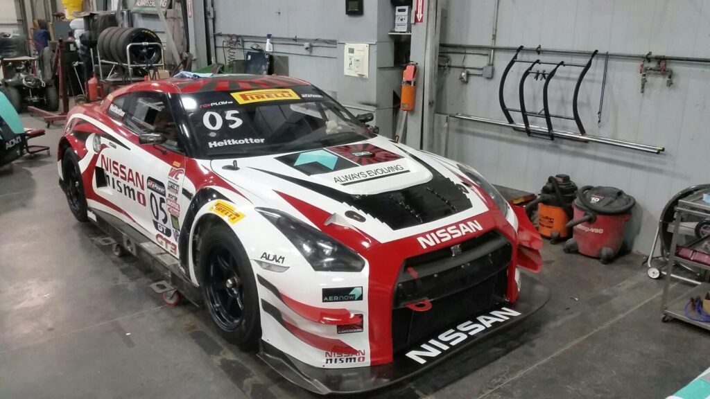Red, white and black Nissan GT-R NISMO GT3 race car with sponsor graphics in the garage