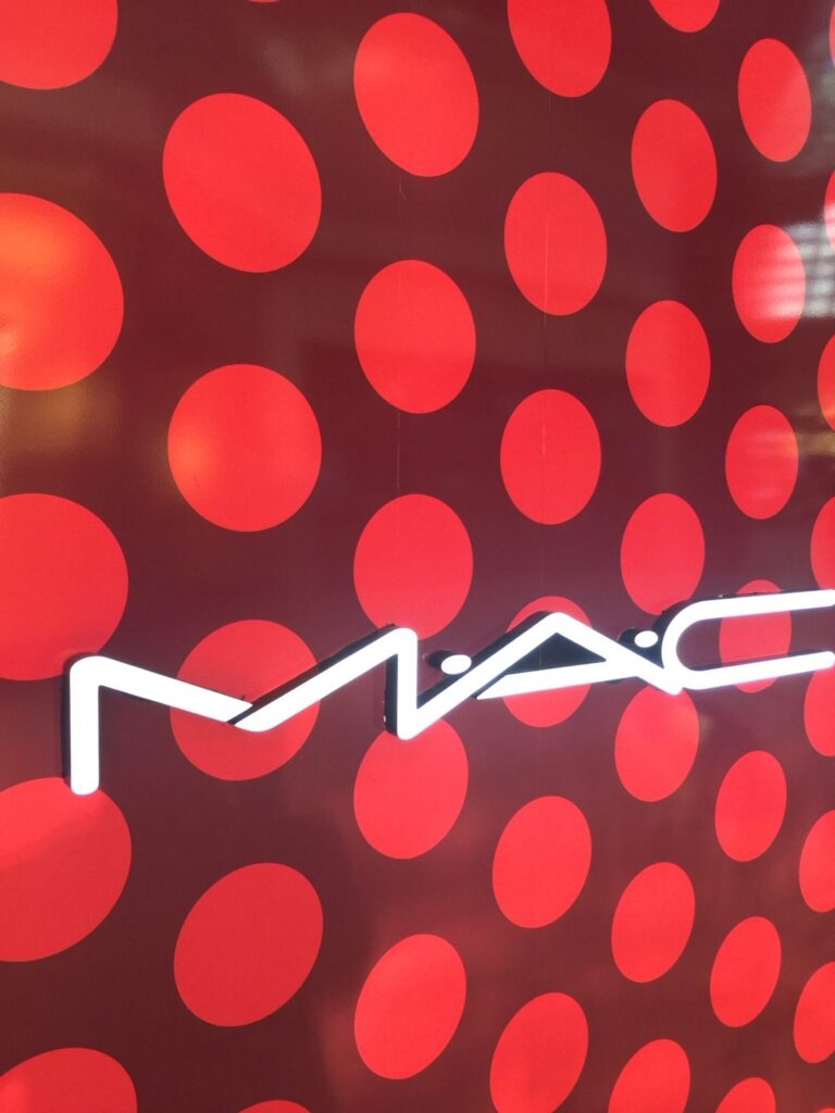 Close-up of illuminated MAC Cosmetics sign over large red dots on burgundy wall graphics