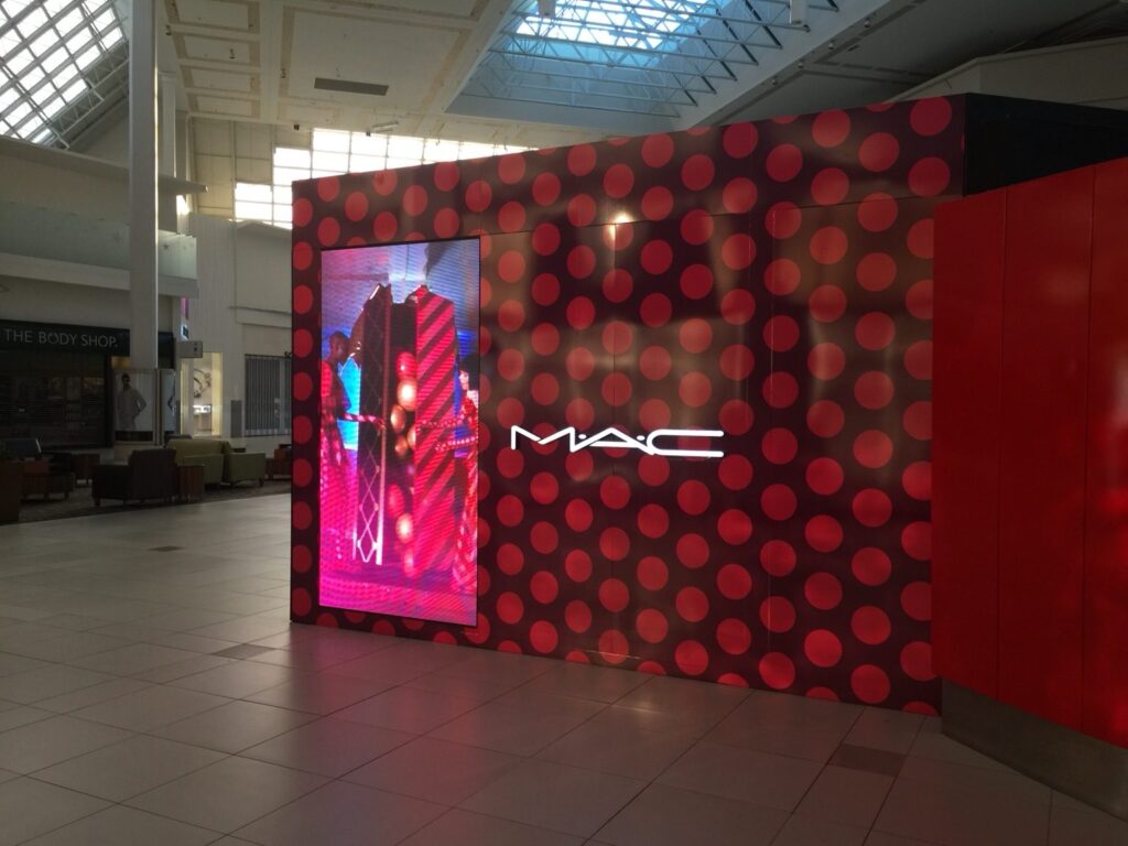 Wide-angle view of MAC Cosmetics branded retail wall installation with digital advertising screen inside The Florida Mall
