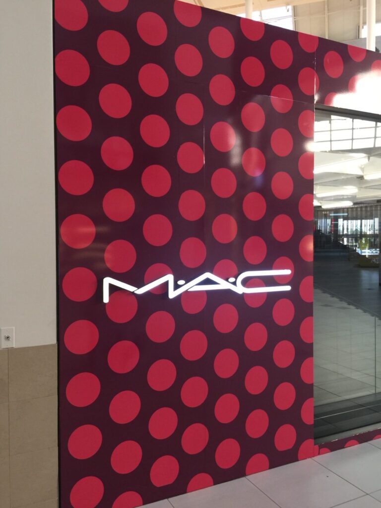 Floor-to-ceiling MAC Cosmetics red circular-pattern wall wrap with illuminated sign beside storefront glazing