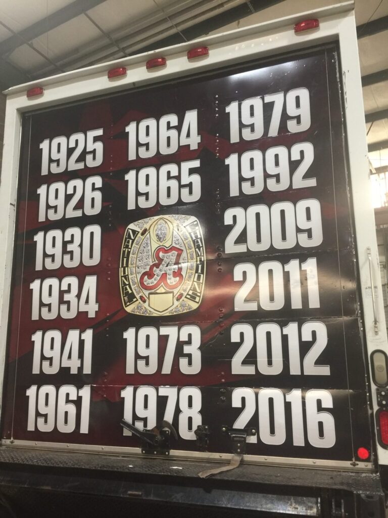Roll-up rear door of a University of Alabama box truck with Alabama football championship years and a championship ring emblem