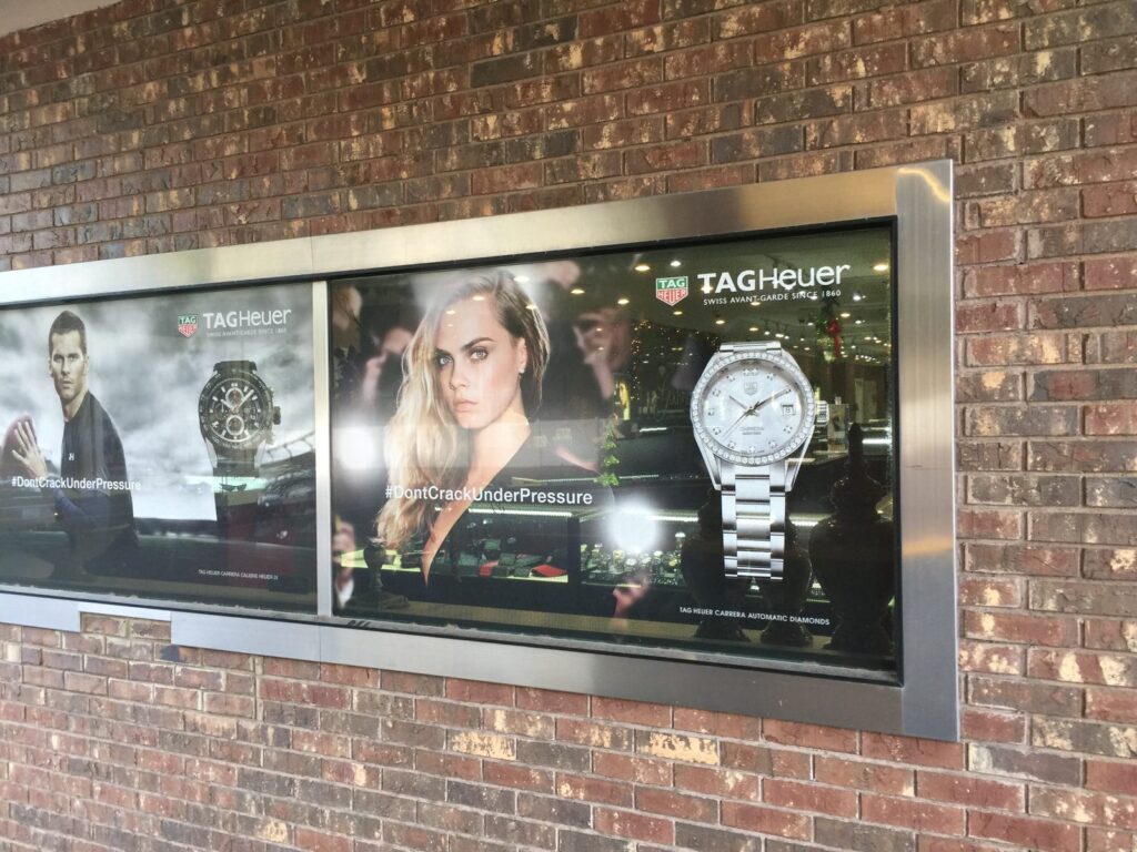 TAG Heuer campaign graphics in an exterior metal-framed display on a brick wall near Bainbridge, Georgia, showing watch imagery and #DontCrackUnderPressure messaging.