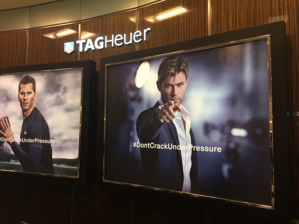 Interior TAG Heuer promotional wall displays in Atlanta: two framed #DontCrackUnderPressure campaign graphics below an illuminated TAG Heuer sign.