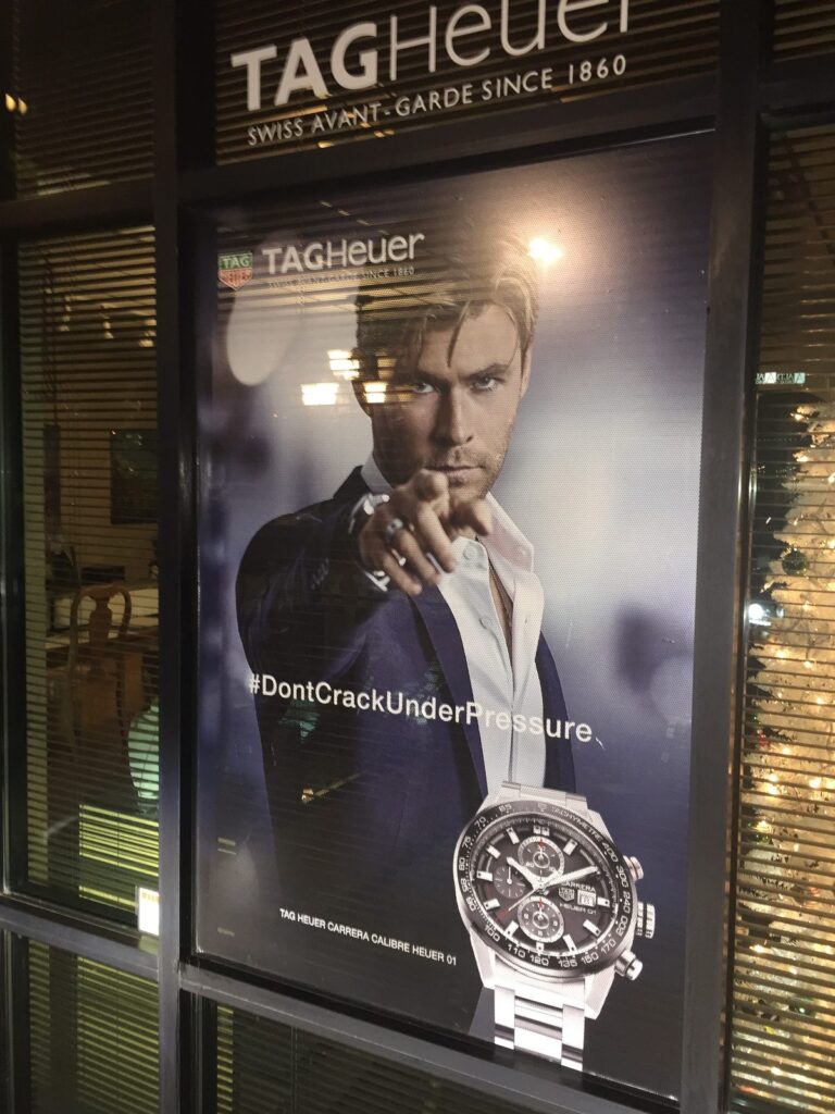 Close-up of a TAG Heuer #DontCrackUnderPressure window graphic near Wichita Falls, Texas, featuring campaign photography and a Carrera Calibre Heuer 01 watch.