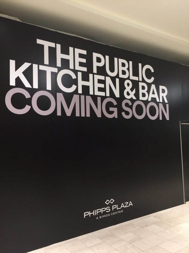 Detail of oversized The Public Kitchen & Bar coming-soon lettering installed on a black retail construction barricade at Phipps Plaza.