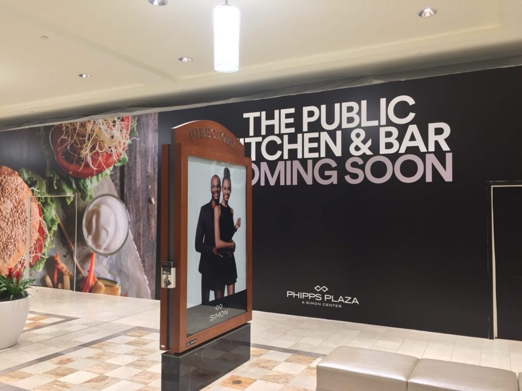 Full-height barricade wrap with food imagery and coming-soon signage for The Public Kitchen & Bar at Phipps Plaza in Atlanta.