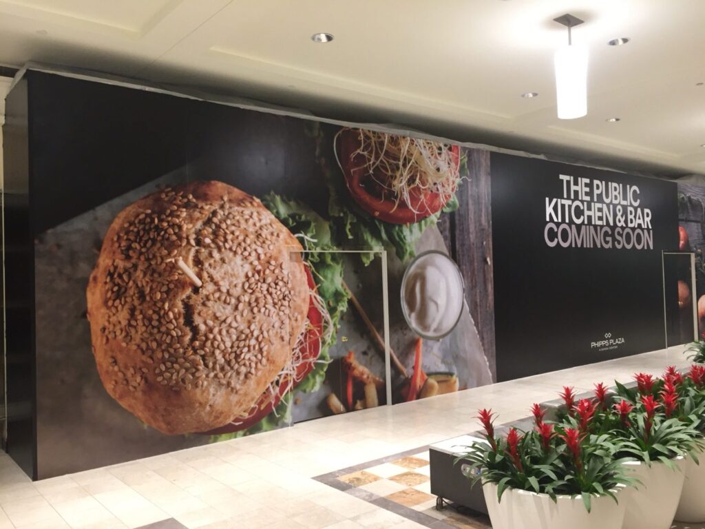 Retail barricade wrap Atlanta: wide view of Black Diamond Designs retail construction barricade graphics for The Public Kitchen & Bar at Phipps Plaza in Atlanta.