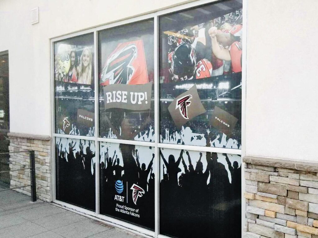 Falcons window graphics seen from the right: RISE UP! panel, AT&T Proud Sponsor of the Atlanta Falcons panel and fan silhouettes across three storefront sections in metro Atlanta.