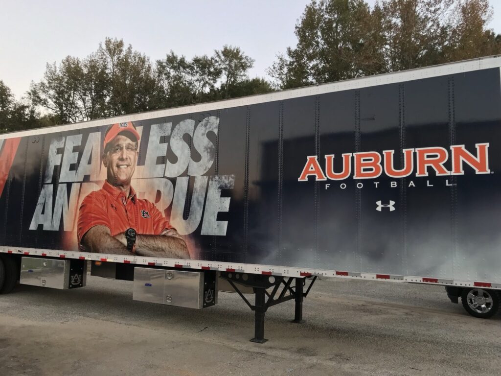 Auburn University football trailer wrap side with Fearless and True lettering, coach portrait, Auburn Football branding, and Under Armour logo at Jordan-Hare Stadium area
