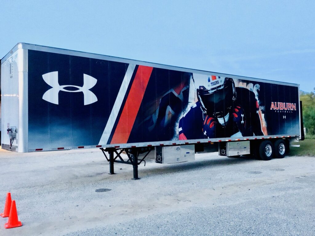 Full-length Auburn Football semi-trailer wrap with Under Armour logo, player imagery, and Auburn Football lettering outdoors
