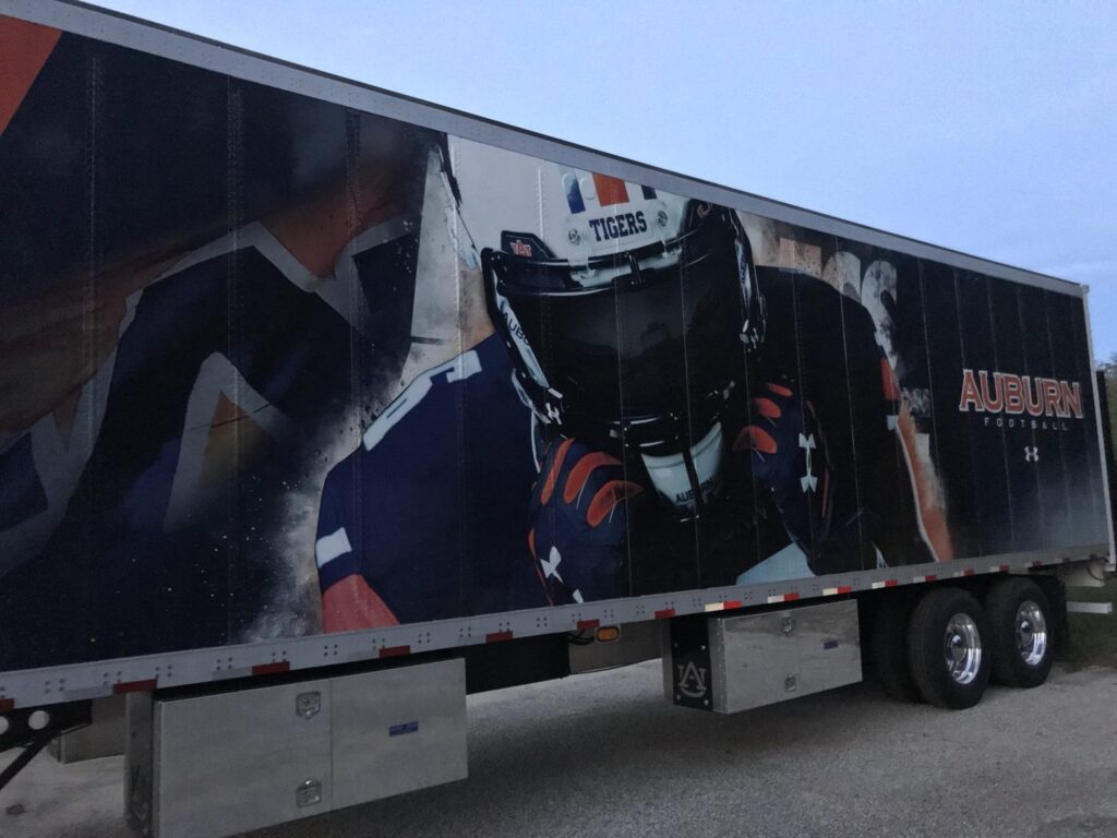 Low-angle view of Auburn Football trailer wrap with player in Tigers helmet, riveted panels, and Under Armour logo