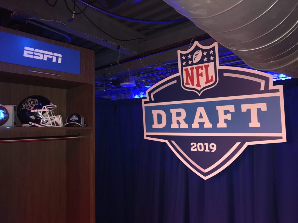 NFL Draft 2019 dimensional logo sign beside an ESPN display with football helmets and caps.