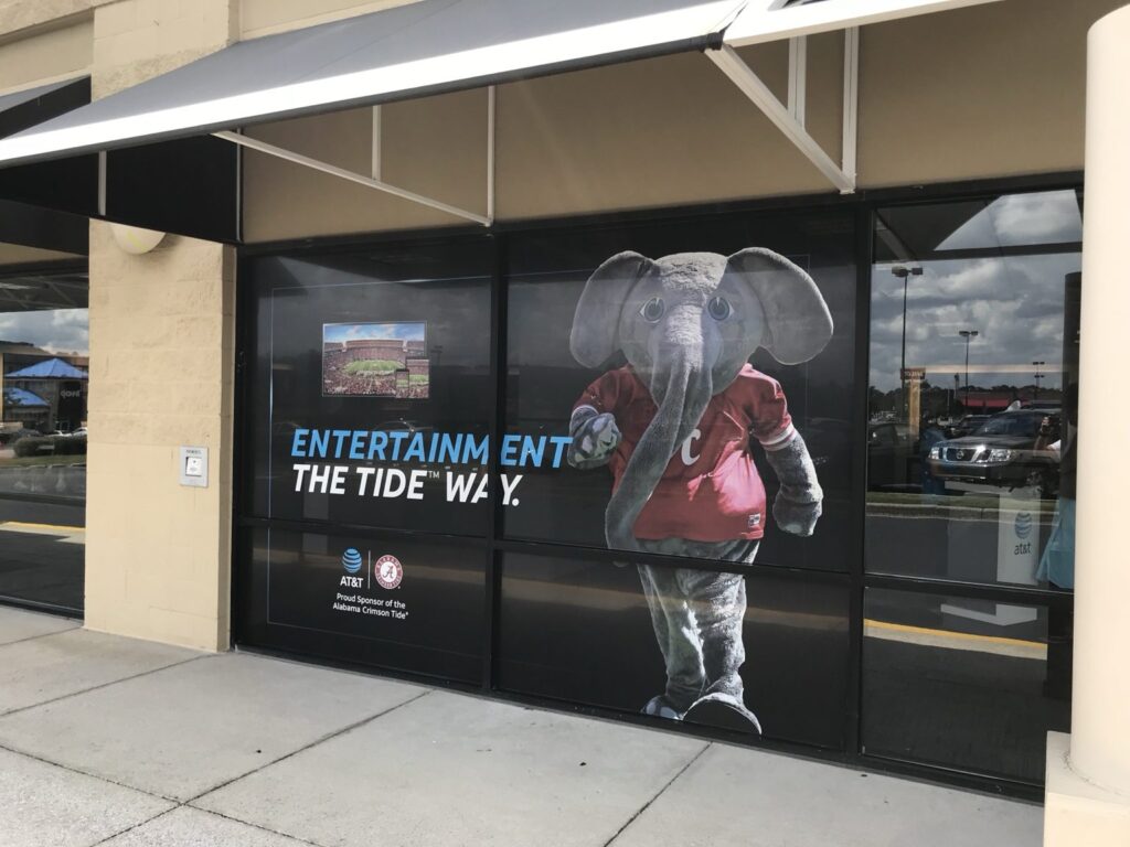 Angled view of dark promotional window graphics spanning an AT&T store frontage in Brook Highland, Birmingham, with an elephant mascot and AT&T sponsorship branding.