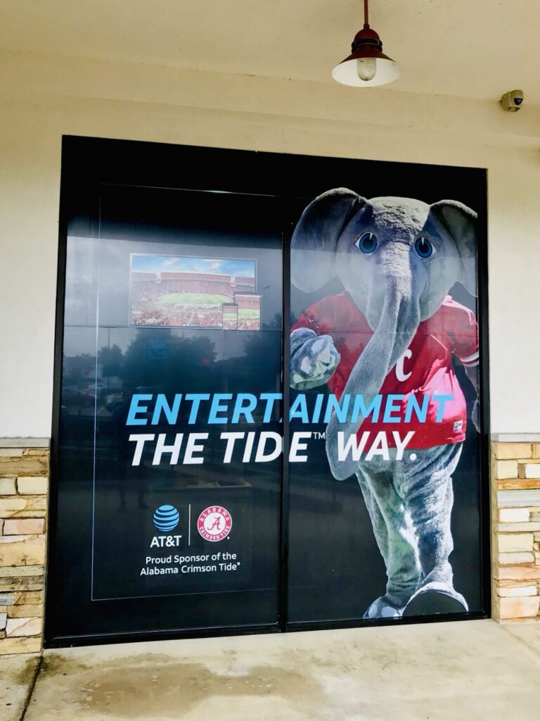 Full-height AT&T Alabama Crimson Tide promotional window graphics featuring the gray elephant mascot in a red jersey beside stadium imagery and AT&T sponsor logos.