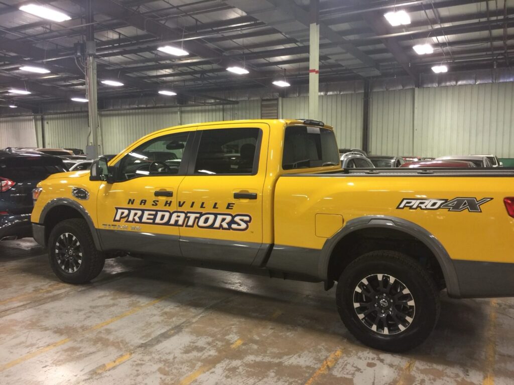 Nashville vehicle graphics installation: bright yellow Nissan Titan XD PRO-4X pickup with Nashville Predators wordmark graphics installed across the doors in an indoor vehicle facility