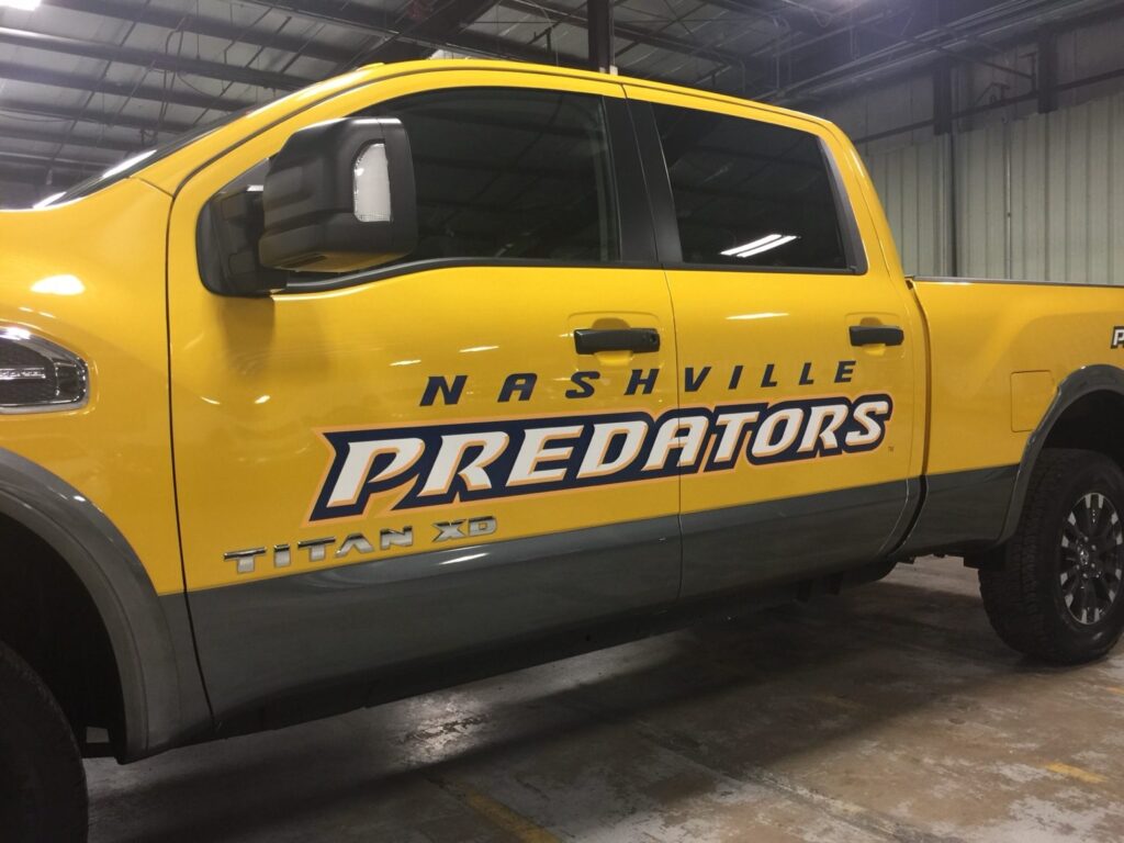Close view of Nashville Predators blue and white door lettering on a yellow Nissan Titan XD pickup truck