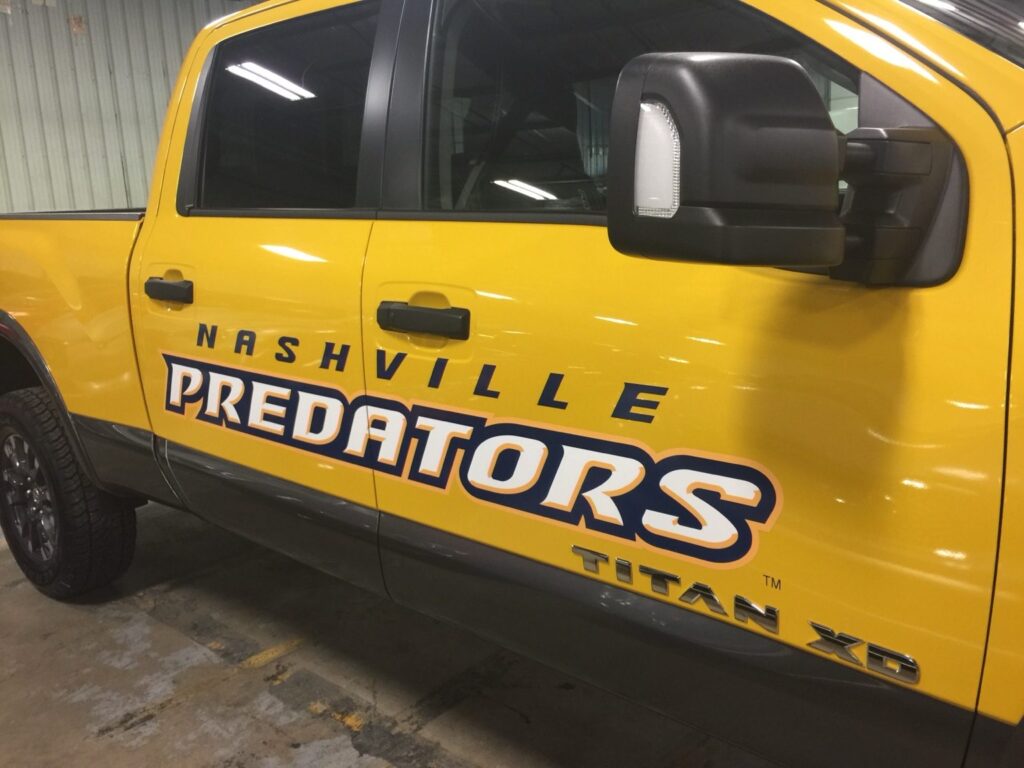 Angled close-up of Nashville Predators lettering positioned across yellow Nissan Titan XD pickup truck doors near black mirror and handles