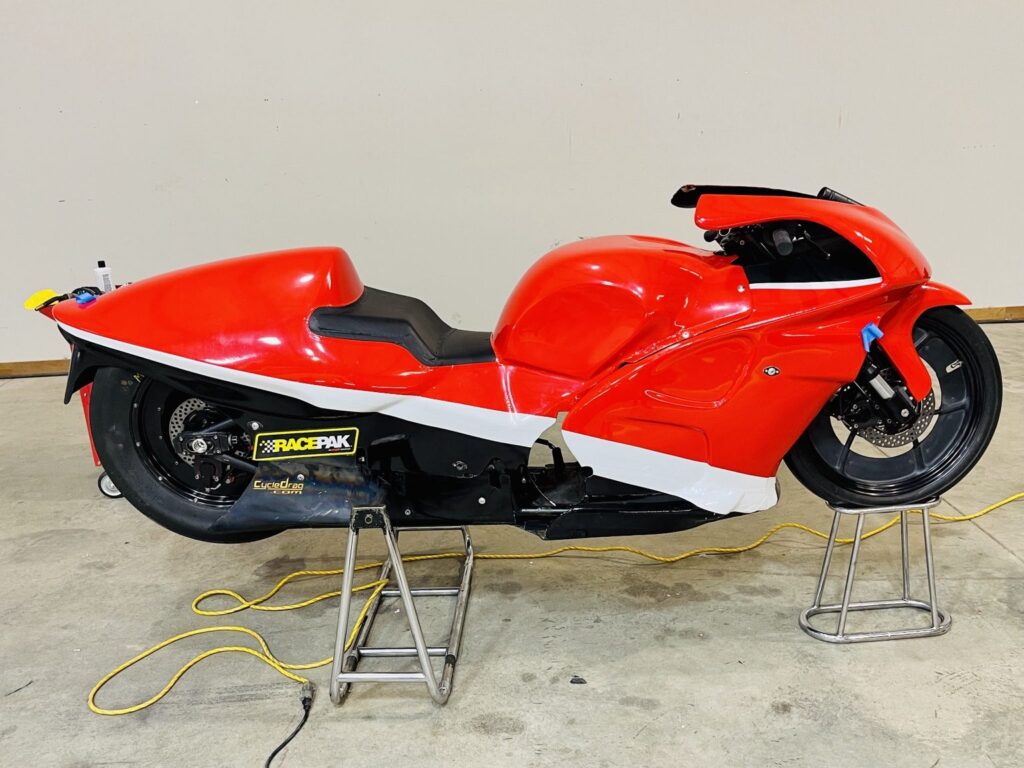 Wide side view of the race bike showing red wrap and white graphics