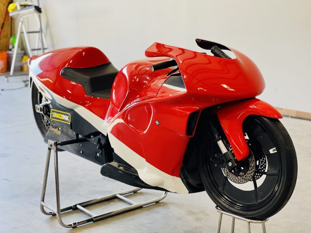 Front three-quarter view of a red Pro Stock drag bike with white stripe and black lower fairing