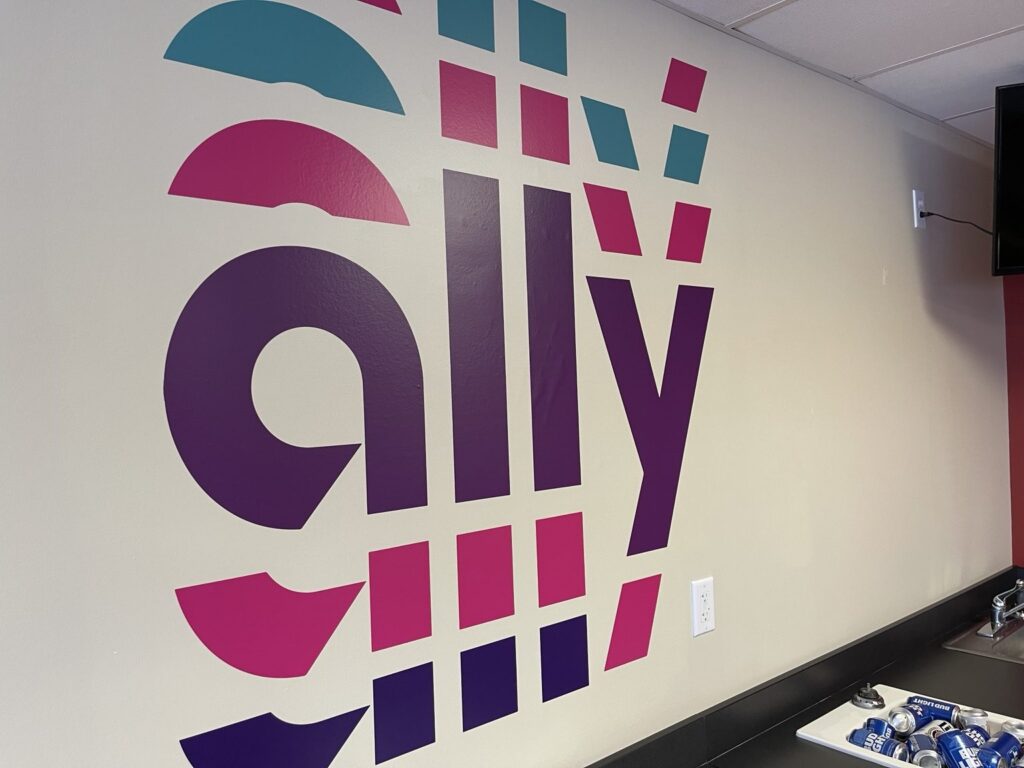 Close-up of a multicolored Ally logo installed on an interior NASCAR suite wall above a refreshment counter