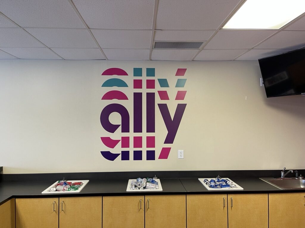Multicolored magenta, teal and purple Ally logo installed above a refreshments counter inside an Atlanta Motor Speedway hospitality suite