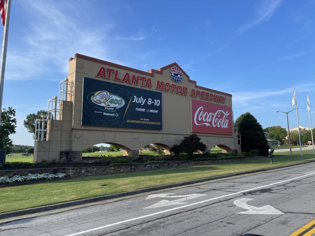 Angled wide view of Atlanta Motor Speedway entrance with July 8–10 Quaker State 400 promotional signage and Coca-Cola panel