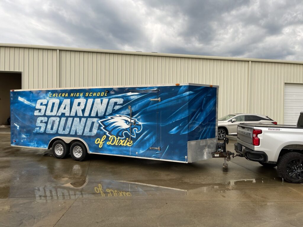 Full side profile of Calera High School marching band cargo trailer wrapped in blue graphics, showing oversized Soaring Sound of Dixie lettering and an eagle mascot.