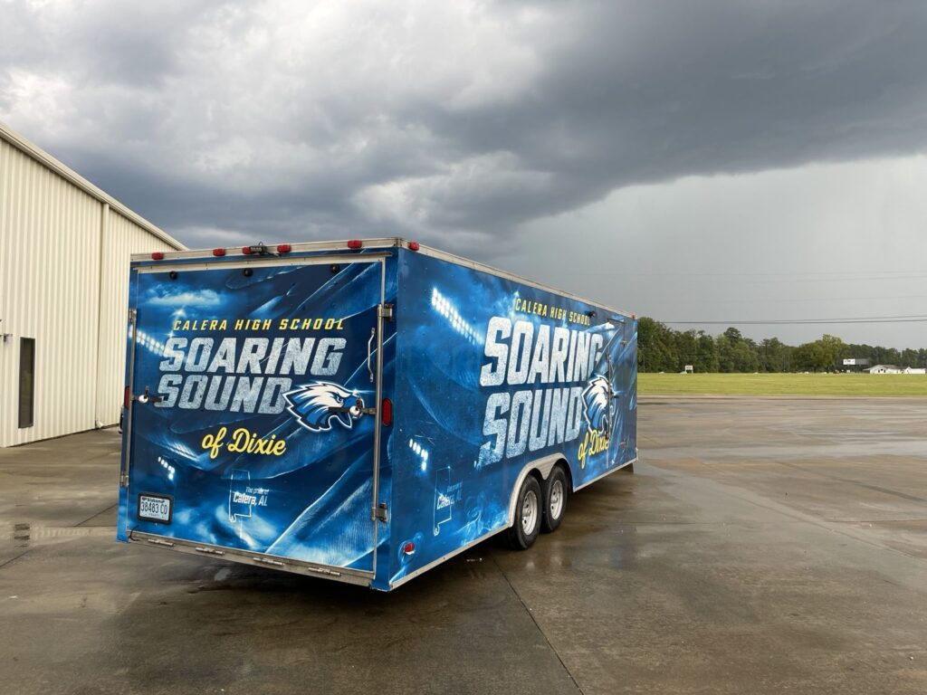 Rear three-quarter view of blue Calera High School Soaring Sound of Dixie marching band cargo trailer wrap, with white lettering, eagle mascot, and Alabama branding.