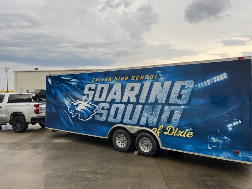 marching band trailer wrap Alabama: large blue Calera High School enclosed band trailer with white Soaring Sound lettering, yellow of Dixie script, eagle mascot and stadium light imagery on the side.