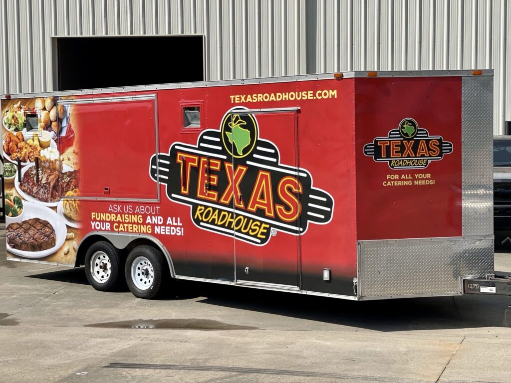 Closer view of the red Texas Roadhouse trailer's large side logo, catering and fundraising copy, food photography and exposed diamond-plate trim.