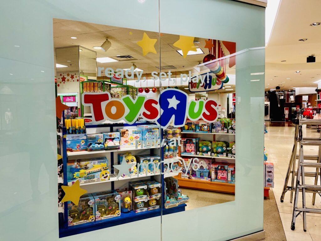 Angled view of Macy's Toys R Us department in Hoover with a pale blue glass surround, colorful Toys R Us logo and ready, set, play graphic.