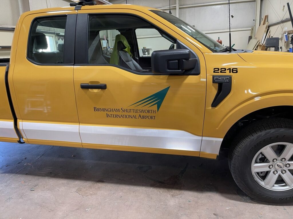 Yellow airport service pickup with logo and partial graphics inside the shop