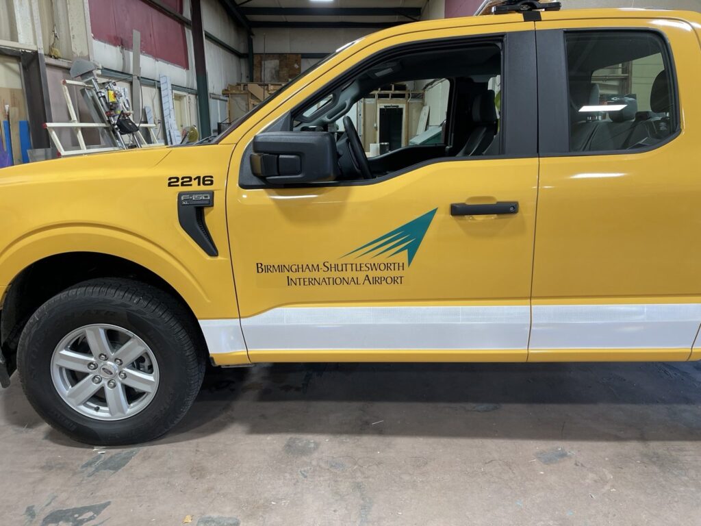 Side detail of service truck 2216 showing the airport logo and white lower-body graphics