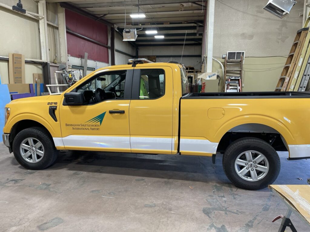Airport service truck graphics Birmingham: full side view of a yellow truck with airport branding and striping