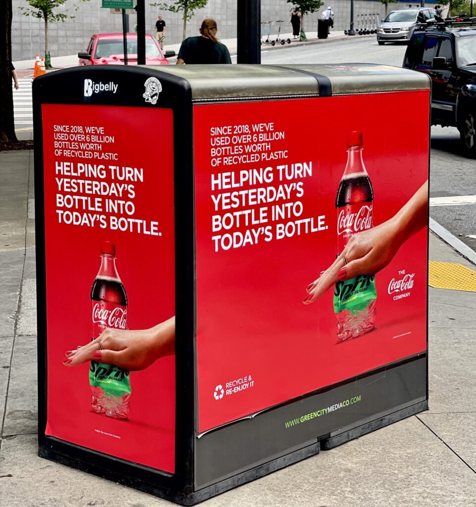 Coca-Cola recycling bin graphics Atlanta: close-up of a red Coca-Cola advertising graphic spanning the front and side panels of a Bigbelly public waste bin in Atlanta.