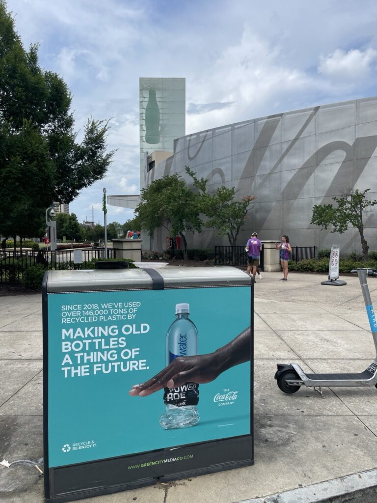 Turquoise Coca-Cola recycled plastic awareness graphic with bottled water imagery installed on a Bigbelly bin along an Atlanta sidewalk.