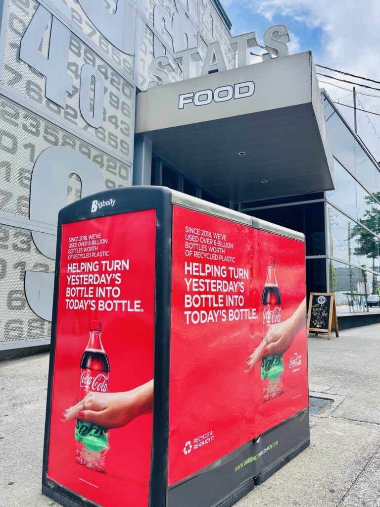 Red Coca-Cola recycling campaign graphics installed on the end and front sides of a Bigbelly bin near STATS Brewpub in Atlanta.