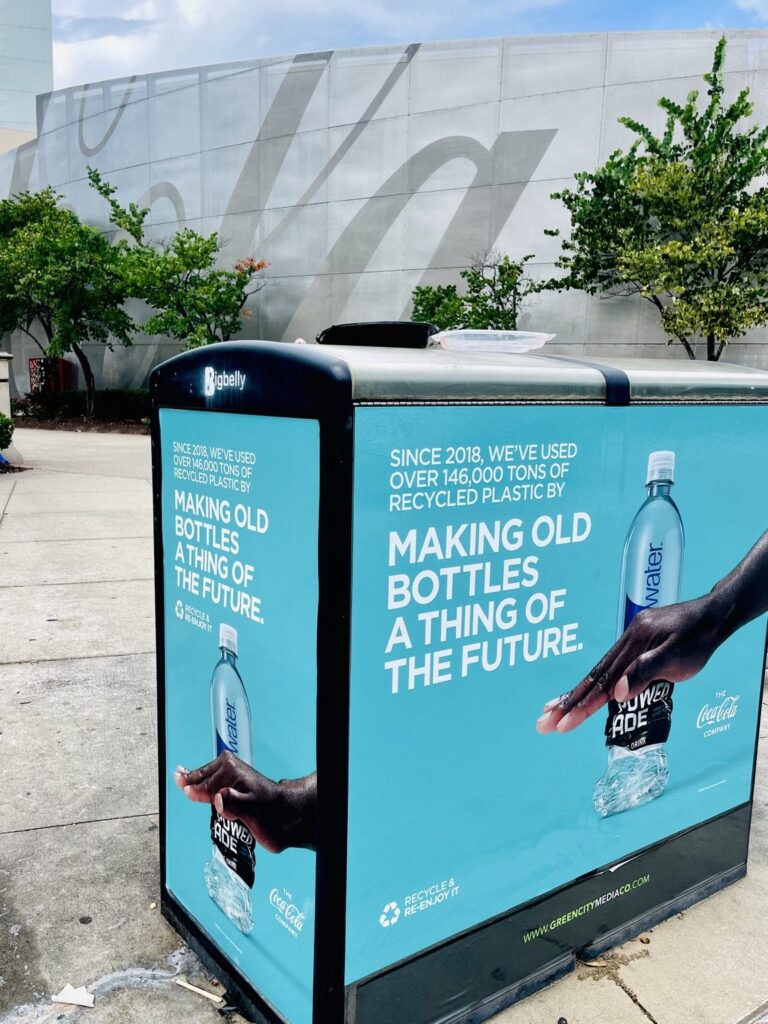 Turquoise Coca-Cola recycling-themed panel graphics with bottle imagery covering the front and end panels of a Bigbelly bin in Atlanta.