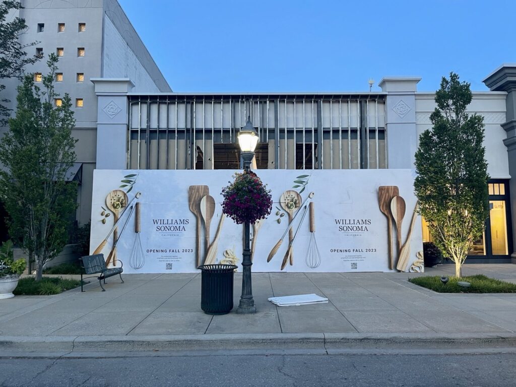 Williams Sonoma barricade wrap Birmingham: wide full-elevation photograph of Williams Sonoma construction barricade graphics at The Summit Birmingham with two branded panels and large kitchen utensil photography.