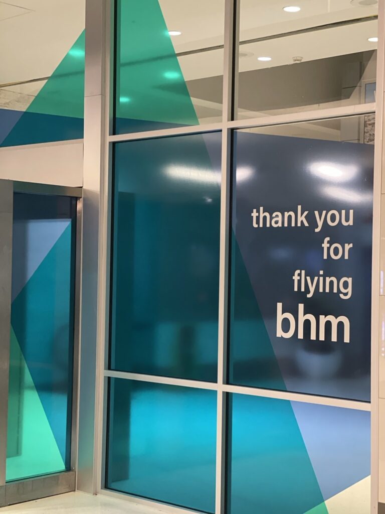 Close view of thank you for flying bhm in white lettering on navy and teal film, framed by the airport's vertical and horizontal window mullions.