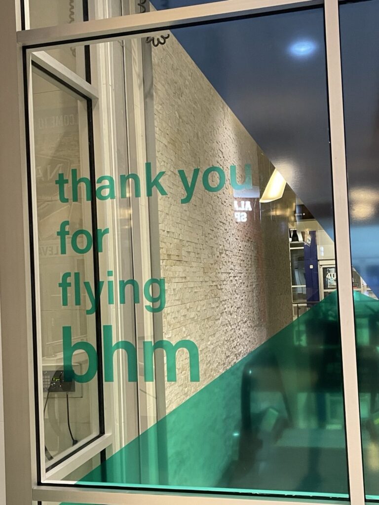 Green thank you for flying bhm lettering viewed through an airport glass panel with teal vinyl and a diagonal navy section.