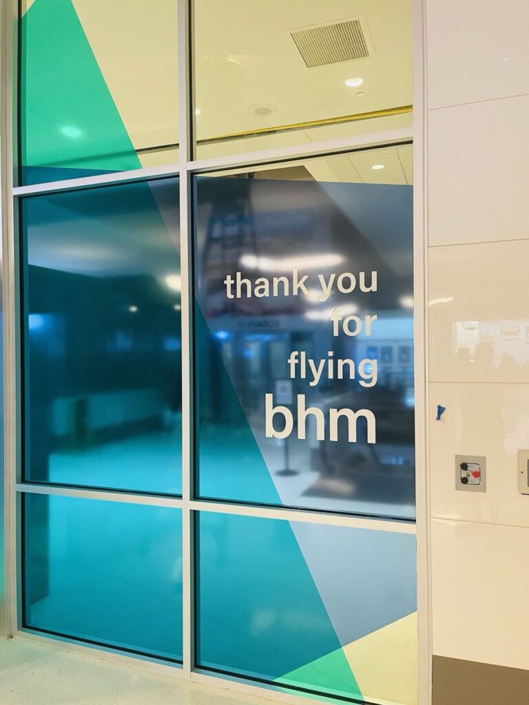 White thank you for flying bhm lettering over navy and teal custom-cut graphic film across large airport glass panels.