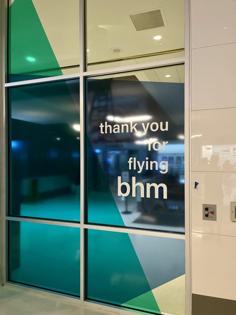 Close-up of white thank you for flying bhm lettering on the airport's blue and green translucent geometric glass graphics.