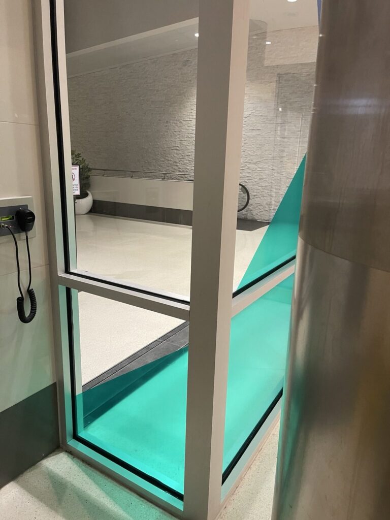 Close view of green translucent geometric film wrapping visually around adjacent glass panes near the airport vestibule.