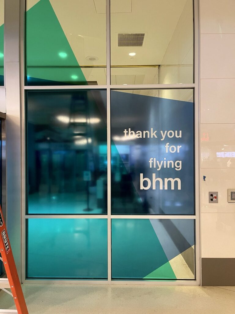 Wide photograph showing teal and navy graphic film across multiple entrance-adjacent glass panels, with thank-you lettering on the right.