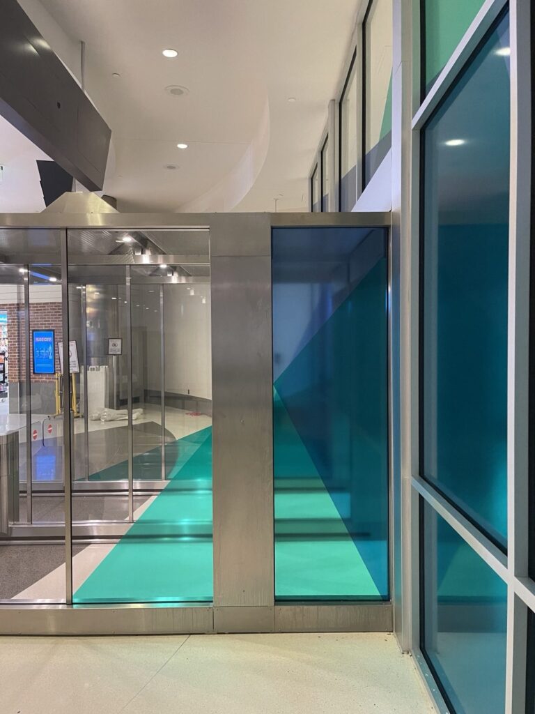 Teal and navy translucent vinyl graphics across interior glass panels beside the airport entrance vestibule in Birmingham, Alabama.