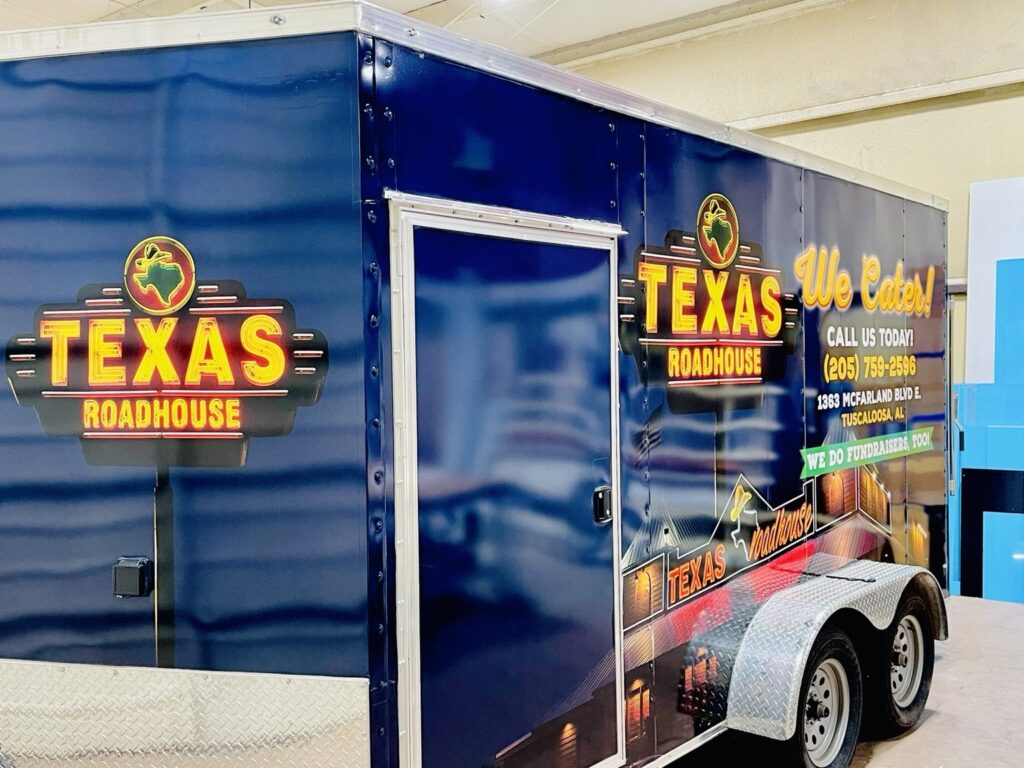 Texas Roadhouse enclosed cargo trailer wrapped in navy 3M IJ180 graphic film with restaurant logos and catering artwork in Birmingham, Alabama.
