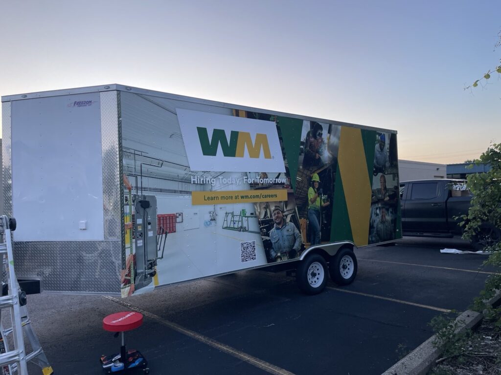 WM cargo trailer during wrap installation, showing hiring artwork and employee photography