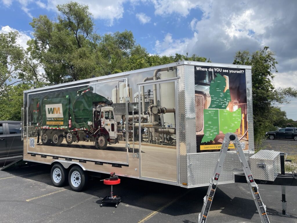 Opposite side of the WM trailer with a garbage truck graphic and green map artwork